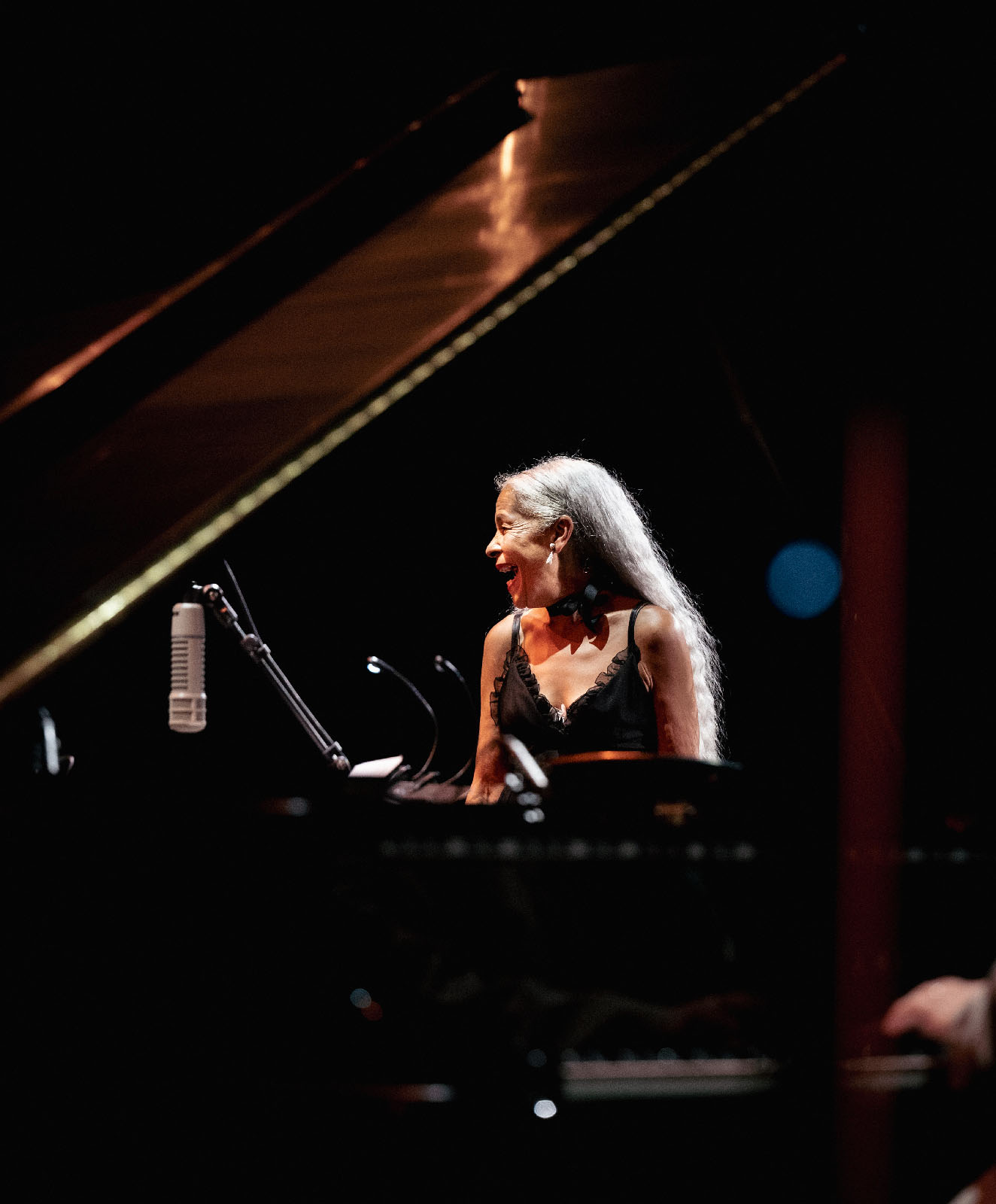 Une femme aux long cheveux gris rit derrière un piano
